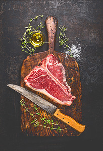 生T骨牛排烧烤烧烤与新鲜草药,油菜刀深色老化的切割板生锈的金属背景,顶部视图图片