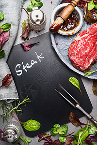 黑板烹饪背景与生牛排,肉叉,新鲜调味料腌制,顶部视图,地点为文本烧烤烧烤的肉类准备图片
