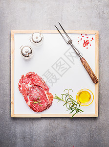 生肉牛排与油,香料肉叉白色厨房托盘上的灰色石头背景,顶部视图,框架图片