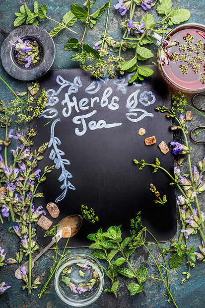 深色黑板上刻上草药茶各种新鲜草药,茶工具杯茶黑暗的复古背景,框架,顶部的健康饮料,排清洁食品的图片