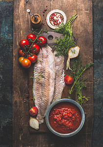 鱼烹饪两个波拉克烤鱼片黑暗的木制背景与番茄酱,新鲜番茄,草药配料,顶部的景观图片