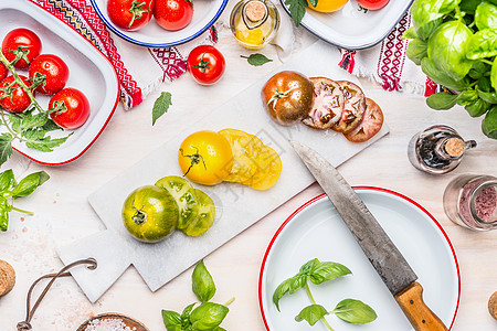 白色厨房桌子上五颜六色的西红柿切片,带刀搪瓷器皿西红柿吃饭西红柿沙拉的各种原料图片
