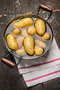 新鲜的新土豆旧平底锅与水乡村木制背景,顶部视图图片