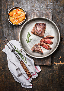 切片中罕见的烤牛排,菲力牛排,金属乡村盘子与肉叉萨尔萨酱黑暗的木制背景,顶部视图图片