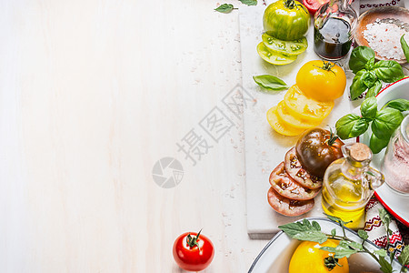 各种五颜六色的西红柿,瓶油沙拉维尼格雷特,罗勒香料白色木制背景,顶部视图,边界图片