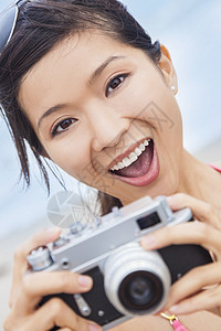 快乐微笑的中国亚洲轻妇女女孩穿着比基尼海滩上用复古数码相机拍照图片