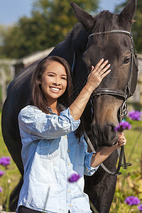 美丽快乐的亚洲欧亚青妇女女孩穿着牛仔衬衫,微笑着带领她的马阳光下图片