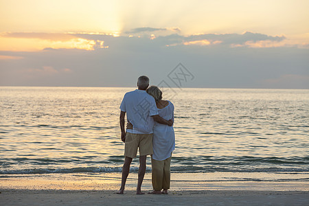老男女夫妇日落日出时拥抱荒芜的热带海滩上图片