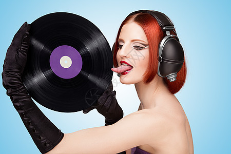 戴着巨大的老式音乐耳机,蓝色背景上舔着紫色的LP微槽乙烯基唱片图片