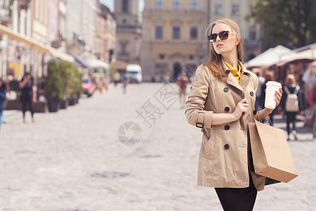 轻的时尚女购物后休息下,城市背景下,手里着咖啡走着图片