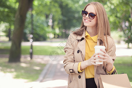 轻时尚的女人购物后休息咖啡,绿色城市公园背景下,手里着咖啡走着图片
