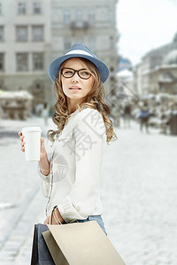 轻时尚的女人,购物袋,购物后喝咖啡,着咖啡杯,城市背景下向边看图片