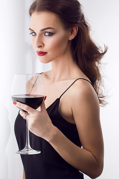 轻漂亮的黑发女人,喝杯红酒图片