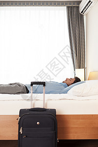 酒店房间里,轻商人躺床上的行李旁边图片