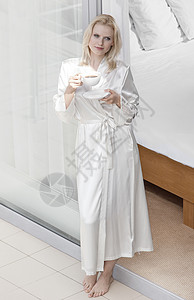 穿着长袍的美丽轻女人阳台门口喝咖啡图片