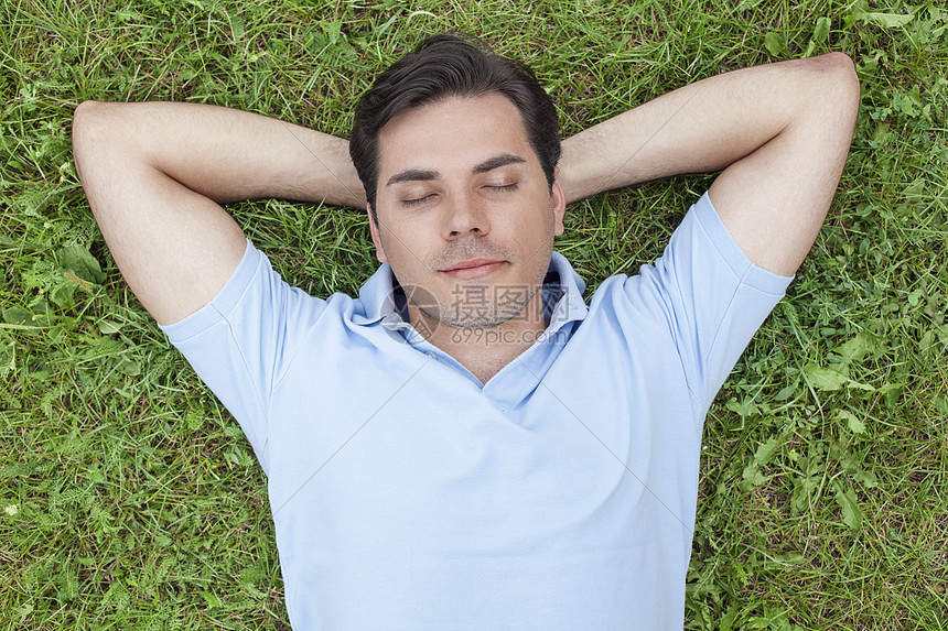 轻人双手抱头躺草地上