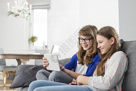 快乐的姐妹们家里的沙发上用数字平板电脑图片