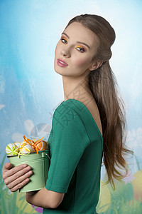 穿着绿色连衣裙的漂亮女孩着桶复活节彩蛋她漂亮的黄色棕色化妆图片