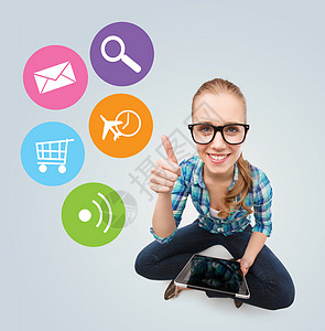 通信技术互联网人的微笑的十几岁女孩戴着眼镜,坐地板上,着灰色背景上的平板电脑,五颜六色的图标图片
