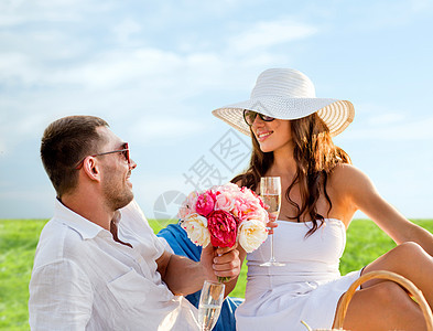 爱情,约会,人假期的微笑的夫妇蓝天草地背景的野餐上喝香槟图片