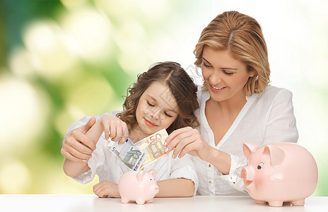 人,财政,家庭预算储蓄快乐的母亲女儿与猪罐纸币绿色背景图片