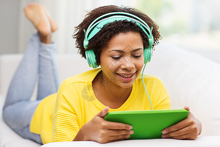 人,技术休闲快乐的非裔美国轻妇女躺沙发上,平板电脑耳机家里听音乐图片