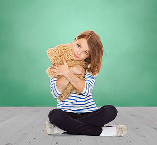 童,学校,玩具人的可爱的小学生女孩拥抱泰迪熊绿色粉笔板背景图片