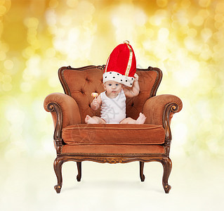 人,童,假日皇室快乐的男孩戴着皇家帽子,棒棒糖坐椅子上的黄色灯光背景图片