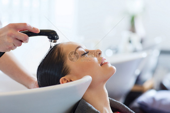 美容人的快乐的轻女人与理发师美发厅洗头图片