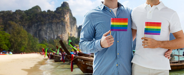 人,同婚姻,旅行爱情亲密的快乐男夫妇手持彩虹旗拥抱泰国海滩背景图片