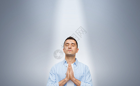 信仰上帝,宗教人的快乐的人,闭着眼睛,灰色背景下的光线下祈祷图片