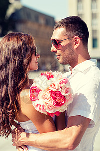 微笑的夫妇戴着太阳镜,带着鲜花拥抱城市里图片