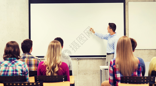 微笑的老师站学生前,教室的白板上写些东西图片