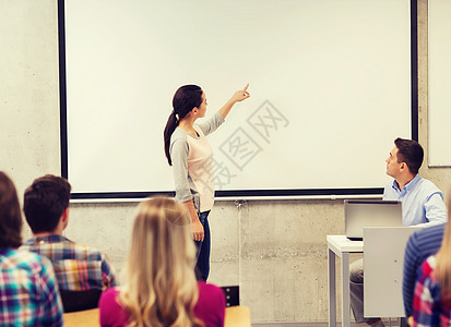 微笑的学生女孩站白板前,老师教室里着笔记本电脑图片