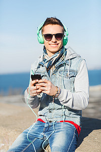 微笑的轻人十几岁的男孩戴着耳机,用智能手机户外听音乐图片