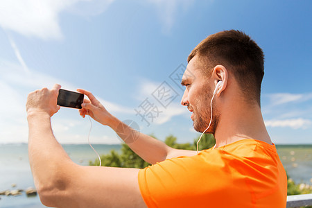 微笑的年轻人与智能手机耳机听音乐夏季海边图片