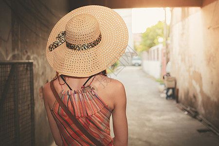 个轻的女人戴着帽子件夏装,日落时站小巷里图片