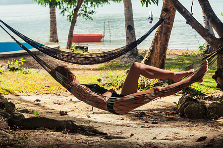 一个年轻的女人正阴凉的热带海滩上的吊床上放松图片