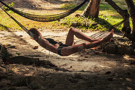 个轻的女人正阴凉的热带海滩上的吊床上放松图片