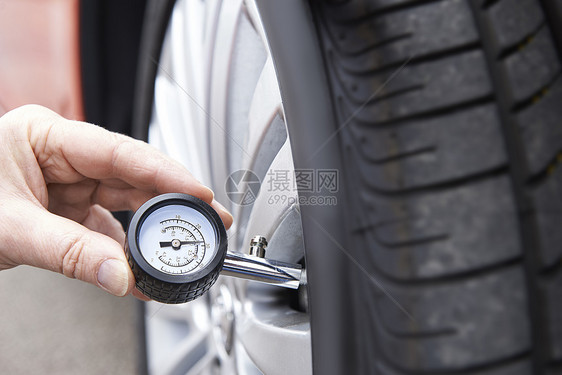 用量规检查汽车轮胎压力的人员特写图片
