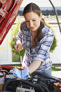 女人用油尺检查引擎盖下的汽车发动机油位图片