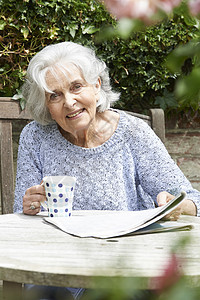 老妇女花园阅读报纸上放松的肖像图片