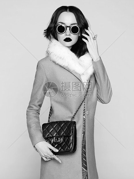 黑白照片,美丽的黑发模特穿着时尚服装摆姿势工作室穿着外套,手提包,太阳镜图片