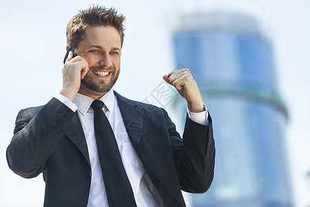个轻的成功人士,男执行商人他的手机上交谈,个现代城市的个高层办公大楼前庆祝图片