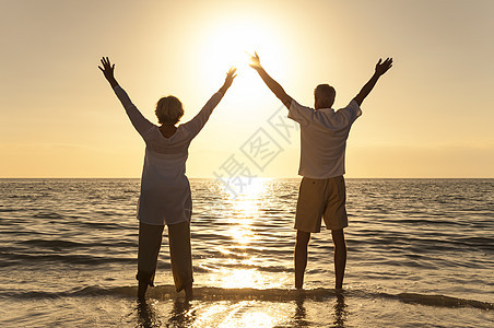 老男女夫妇举双臂,日落日出时美丽的热带海滩上庆祝图片
