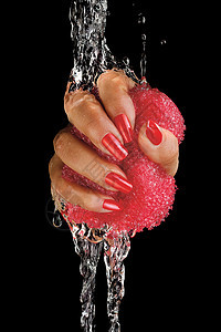 只雌晒黑的手的特写,画着指甲,水流中拧着粉红色的海绵图片