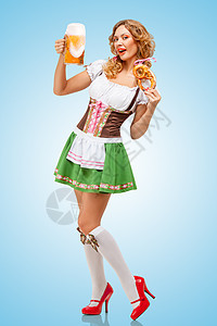 轻感的啤酒节女服务员穿着传统的巴伐利亚连衣裙,蓝色背景上提供椒盐卷饼啤酒杯图片