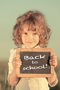 快乐微笑的小学生着小黑板,带着课文回学校天空的背景下图片