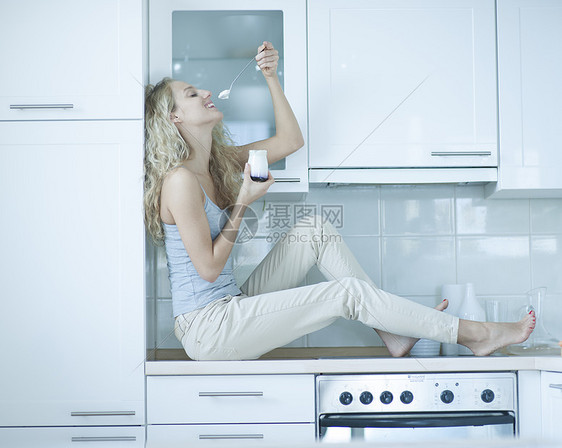 轻女人坐厨房柜台上吃酸奶的侧视图片