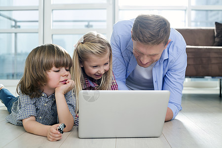 家庭场景快乐的父亲孩子们客厅的地板上用笔记本电脑背景